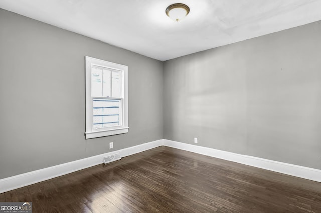 unfurnished room with baseboards, visible vents, and dark wood-type flooring