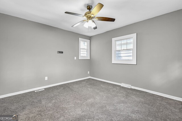 spare room with a ceiling fan, dark carpet, visible vents, and baseboards