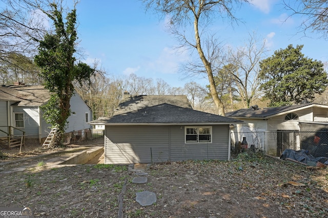 rear view of house featuring roof with shingles and fence