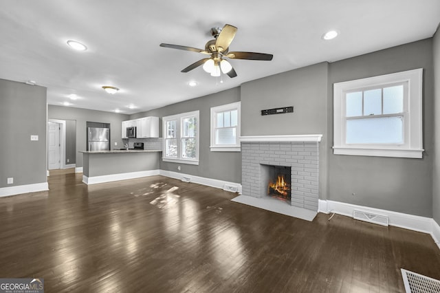 unfurnished living room featuring a brick fireplace, visible vents, dark wood finished floors, and baseboards