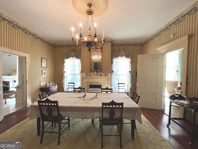 dining area with wood finished floors, a fireplace, an inviting chandelier, and wallpapered walls