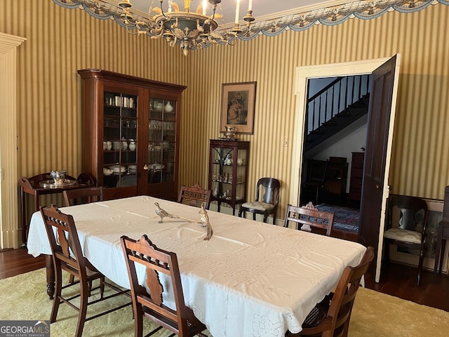 dining space featuring wallpapered walls, a notable chandelier, stairs, and wood finished floors