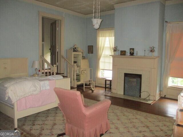 bedroom featuring ornamental molding, a brick fireplace, and wood finished floors