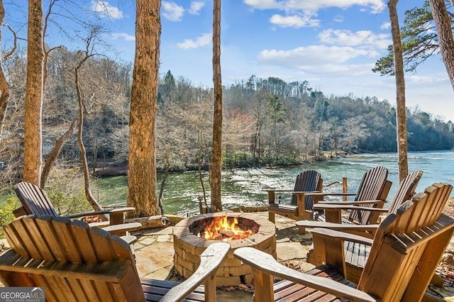 view of patio featuring an outdoor fire pit, a water view, and a wooded view