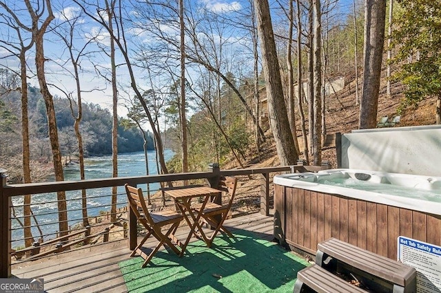 wooden deck with a view of trees, a water view, and a hot tub