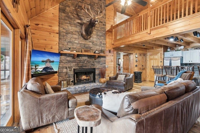 living room with a ceiling fan, a stone fireplace, wooden walls, wood finished floors, and high vaulted ceiling