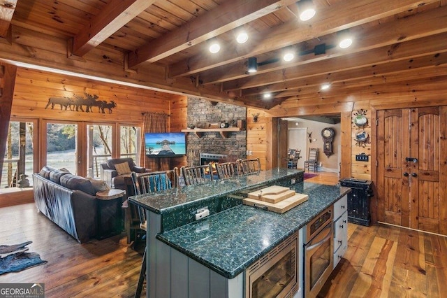 kitchen with beam ceiling, a fireplace, stainless steel appliances, wood walls, and hardwood / wood-style floors