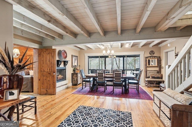 dining room featuring a lit fireplace, light wood finished floors, beam ceiling, and a notable chandelier