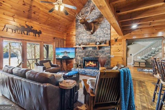 living room with high vaulted ceiling, a stone fireplace, wooden walls, stairs, and hardwood / wood-style floors