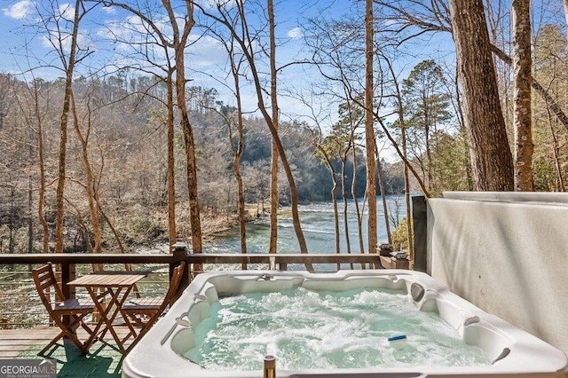 deck with a water view, a hot tub, and a wooded view