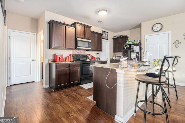 kitchen with black appliances, a kitchen bar, visible vents, and dark wood-style flooring