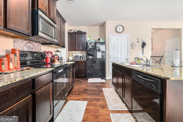 kitchen featuring dark wood finished floors, light stone countertops, dark brown cabinets, black appliances, and a sink