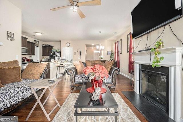 living room featuring ceiling fan with notable chandelier, a glass covered fireplace, baseboards, and wood finished floors