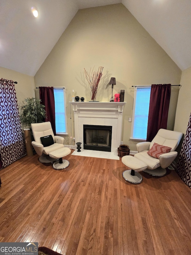 sitting room featuring high vaulted ceiling, wood-type flooring, a fireplace with flush hearth, and a wealth of natural light