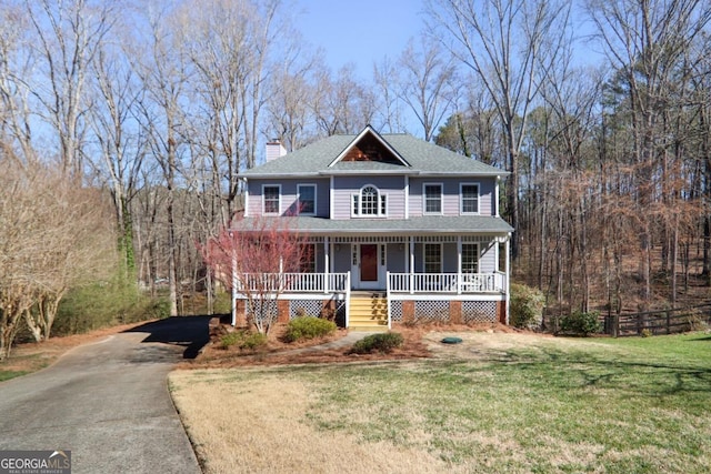 view of front of house featuring a forest view, a chimney, aphalt driveway, a porch, and a front yard