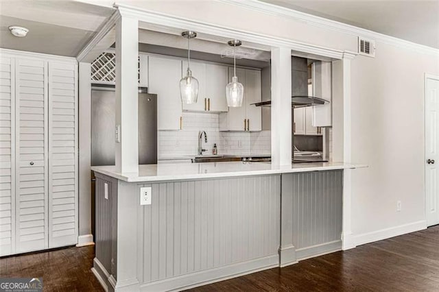 kitchen featuring light countertops, dark wood finished floors, a peninsula, and wall chimney exhaust hood