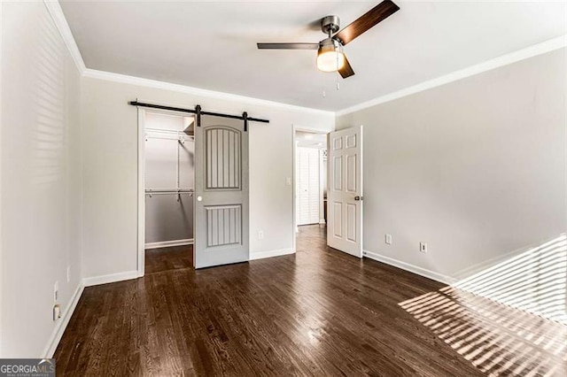 unfurnished bedroom featuring crown molding, a spacious closet, a barn door, wood finished floors, and baseboards