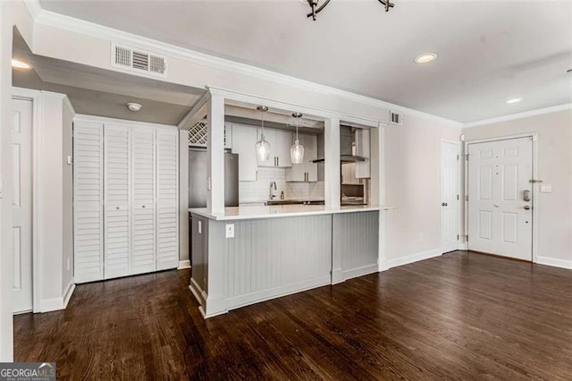 kitchen with dark wood-type flooring, visible vents, light countertops, ornamental molding, and wall chimney exhaust hood