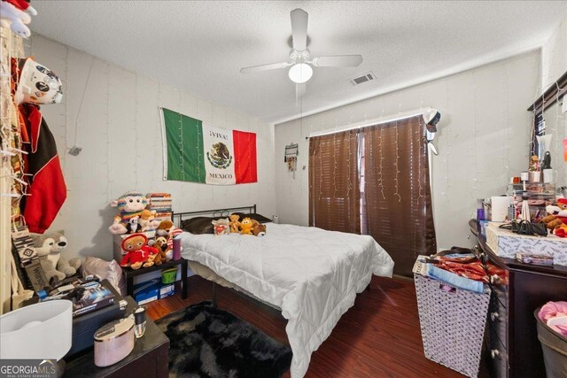 bedroom with ceiling fan, a textured ceiling, visible vents, and wood finished floors