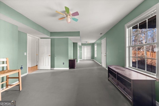 living area with concrete flooring, ceiling fan, and baseboards