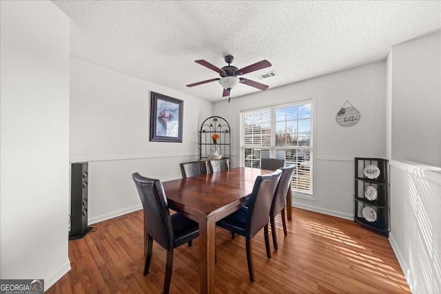 dining area featuring visible vents, ceiling fan, a textured ceiling, wood finished floors, and baseboards