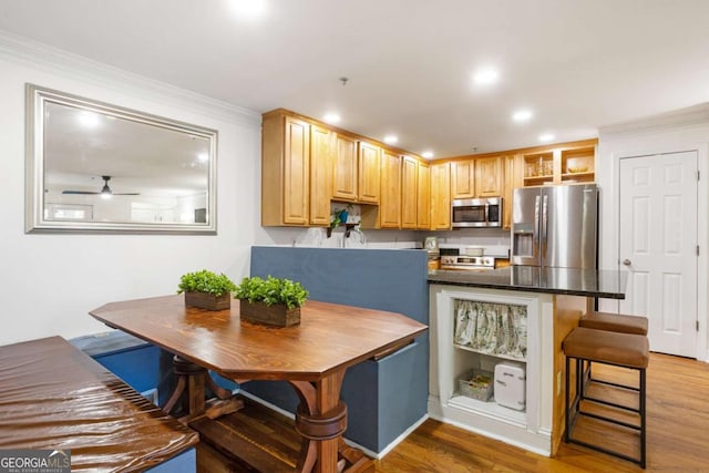 kitchen featuring appliances with stainless steel finishes, dark countertops, light wood-style floors, and a kitchen breakfast bar