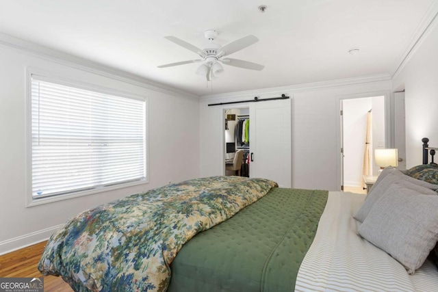 bedroom with a barn door, wood finished floors, baseboards, ornamental molding, and a walk in closet