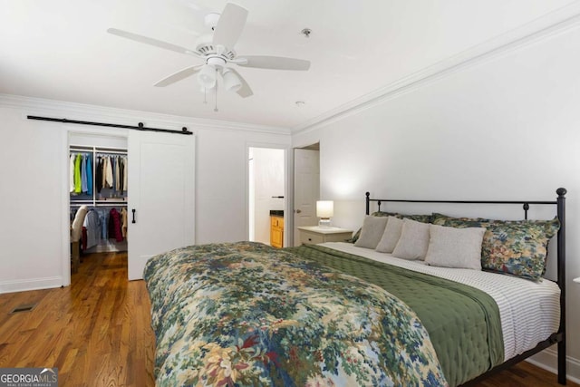 bedroom with crown molding, a closet, a spacious closet, a barn door, and wood finished floors