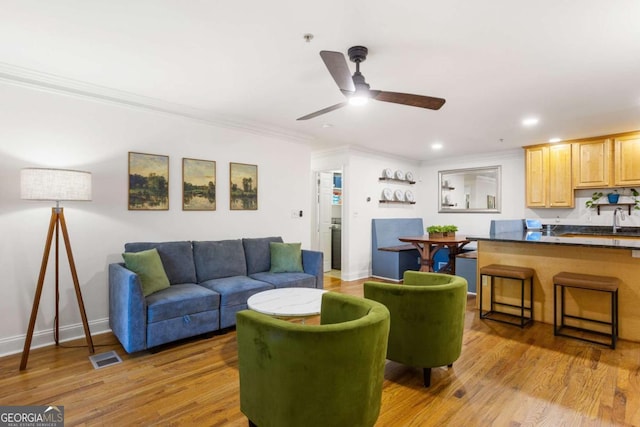 living area featuring light wood-style flooring, visible vents, baseboards, and ornamental molding