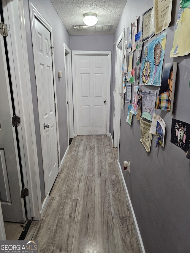 hall featuring visible vents, a textured ceiling, baseboards, and wood finished floors