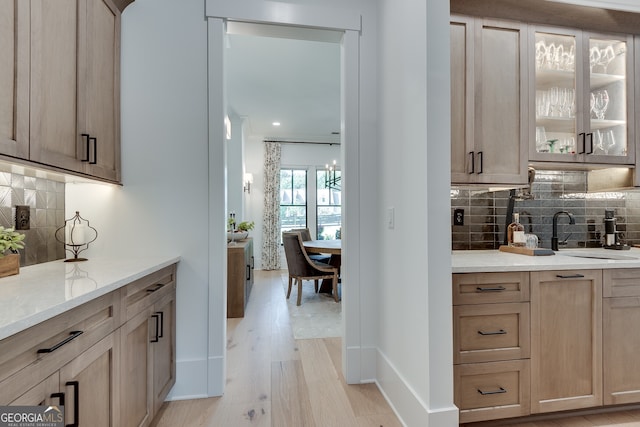 bar with baseboards, decorative backsplash, a sink, and light wood-style floors