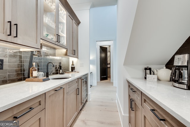 kitchen with a sink, baseboards, light countertops, decorative backsplash, and glass insert cabinets