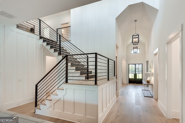 entrance foyer featuring light wood-type flooring, visible vents, a decorative wall, and a towering ceiling