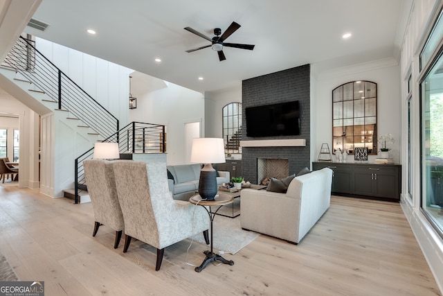 living area with ceiling fan, visible vents, stairway, a brick fireplace, and light wood finished floors