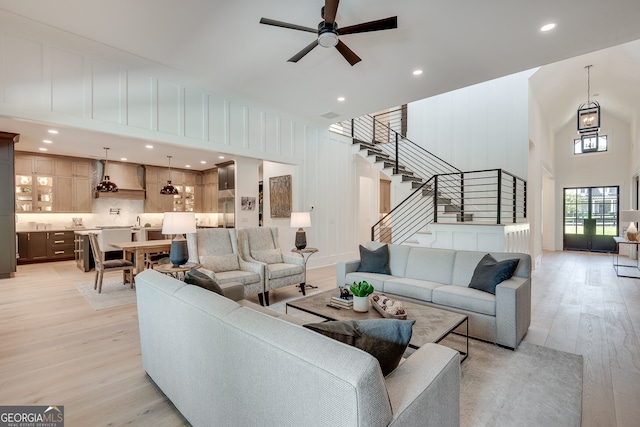 living area with light wood finished floors, a towering ceiling, ceiling fan, stairway, and a decorative wall