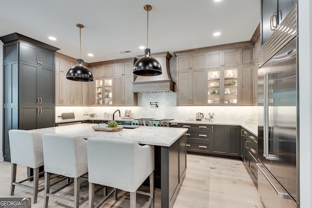 kitchen featuring a center island with sink, visible vents, light stone counters, custom exhaust hood, and a sink