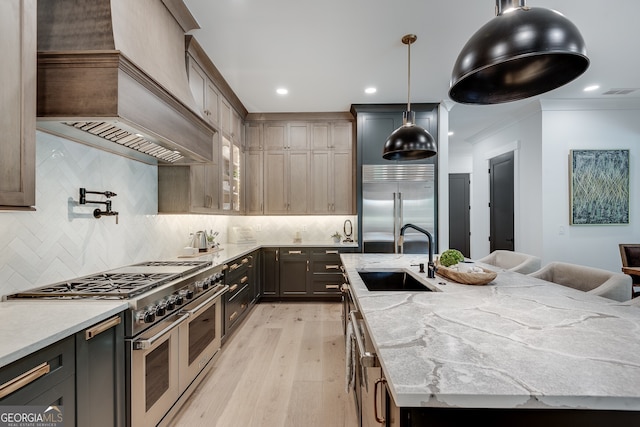 kitchen featuring light wood-style flooring, premium range hood, a spacious island, a sink, and high quality appliances