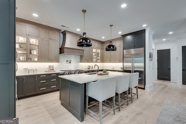 kitchen featuring decorative backsplash, a breakfast bar area, a kitchen island with sink, stainless steel appliances, and premium range hood