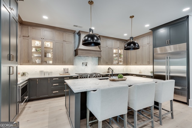 kitchen with visible vents, a breakfast bar, built in appliances, light stone countertops, and a sink