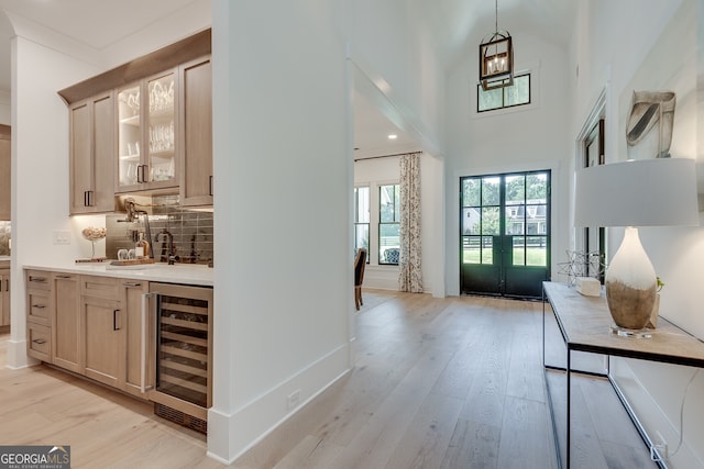 entrance foyer featuring wine cooler, a towering ceiling, light wood-style flooring, wet bar, and baseboards