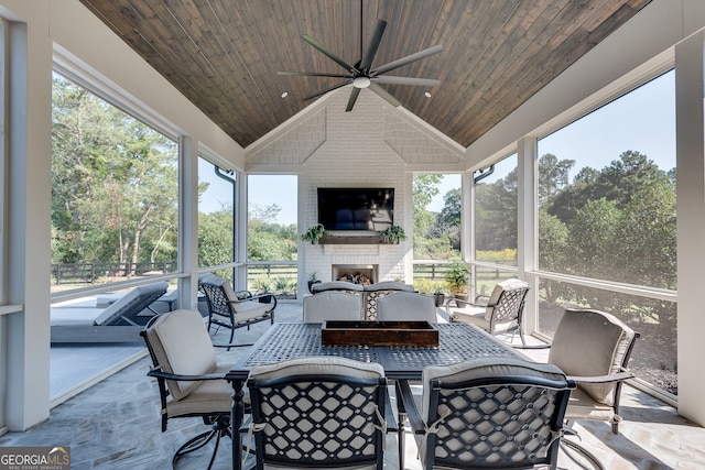 sunroom with vaulted ceiling, ceiling fan, an outdoor brick fireplace, and wood ceiling