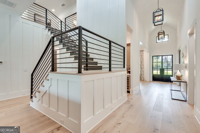 entryway with visible vents, a towering ceiling, a decorative wall, stairway, and light wood finished floors