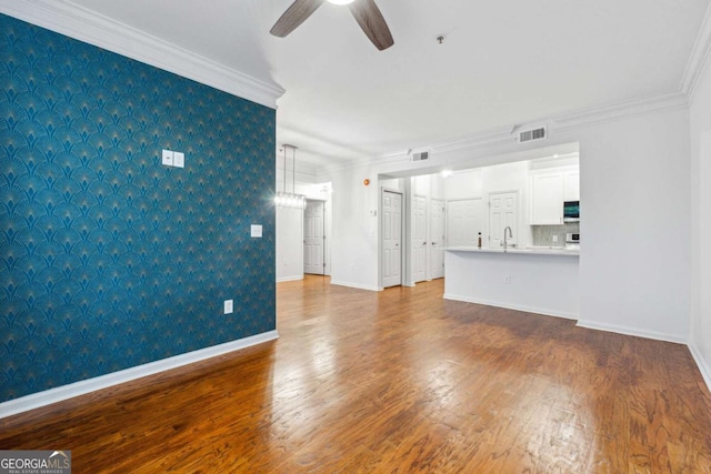 unfurnished living room featuring wallpapered walls, baseboards, visible vents, and crown molding