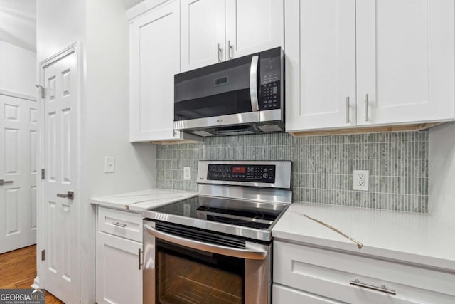 kitchen featuring appliances with stainless steel finishes, white cabinets, light stone counters, and tasteful backsplash