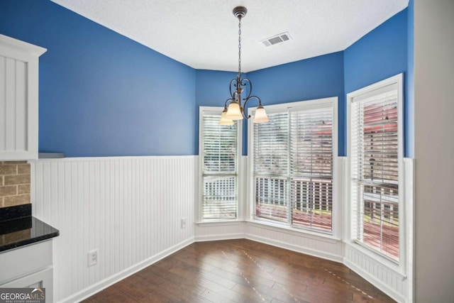 unfurnished dining area featuring a wealth of natural light, a notable chandelier, dark wood-type flooring, and a wainscoted wall