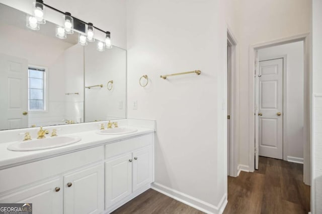 bathroom with double vanity, wood finished floors, a sink, and baseboards