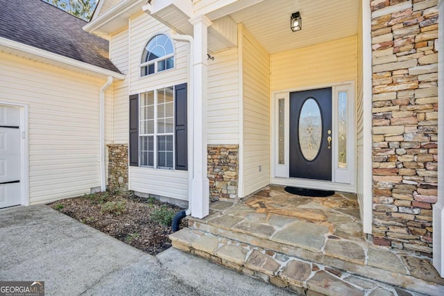 entrance to property featuring a shingled roof, stone siding, a porch, and an attached garage