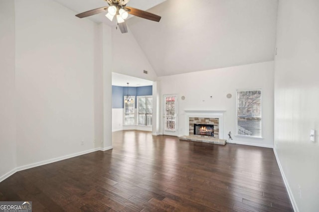 unfurnished living room featuring ceiling fan with notable chandelier, a stone fireplace, baseboards, and wood finished floors