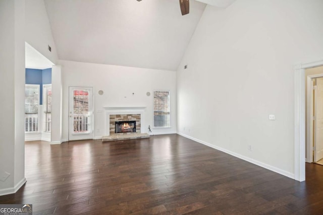 unfurnished living room featuring high vaulted ceiling, a stone fireplace, dark wood-style flooring, and baseboards