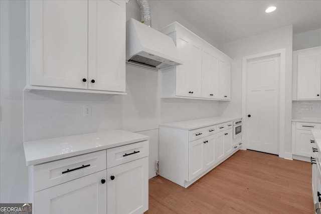 kitchen featuring tasteful backsplash, light countertops, white cabinetry, light wood-type flooring, and premium range hood